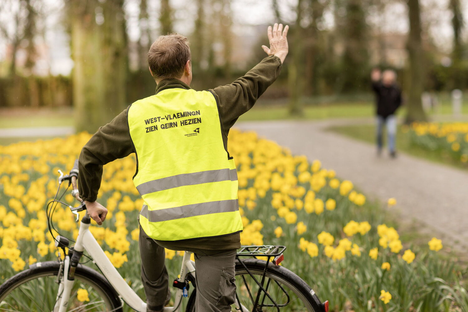 Fietser met fluo jas zwaait naar een voetganger