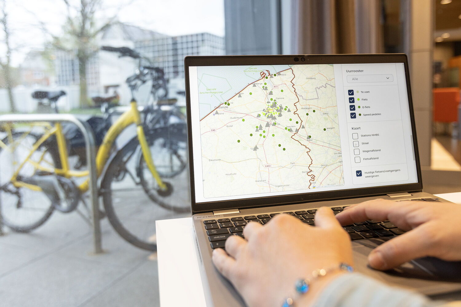 Persoon bekijkt mobiscan. Achter laptop staan er buiten fietsen.